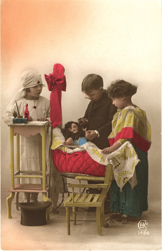 Weiße Kinder, gekleidet als Krankenschwester, Arzt und Mutter. Alle stehen über einer Puppe in einem Kinderbett.
